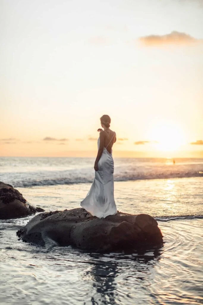 Woman in white dress standing on a rock in water