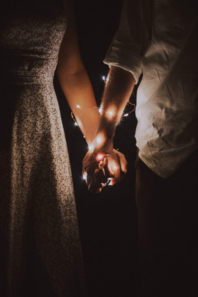 Couple holding hands with fairy lights wrapped around