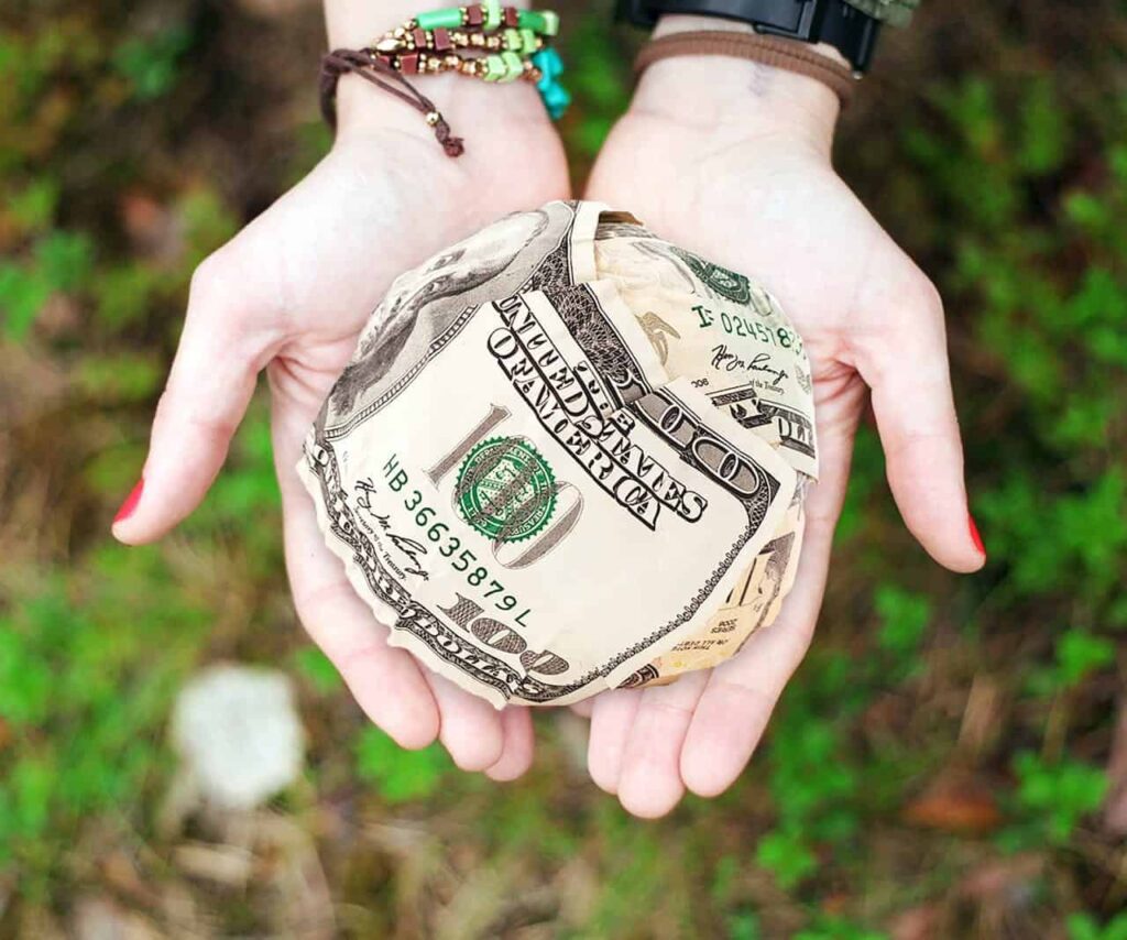 Person holding a ball of hundred dollar bills