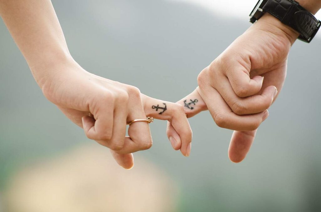 Couple with matching anchor tattoos holding fingers