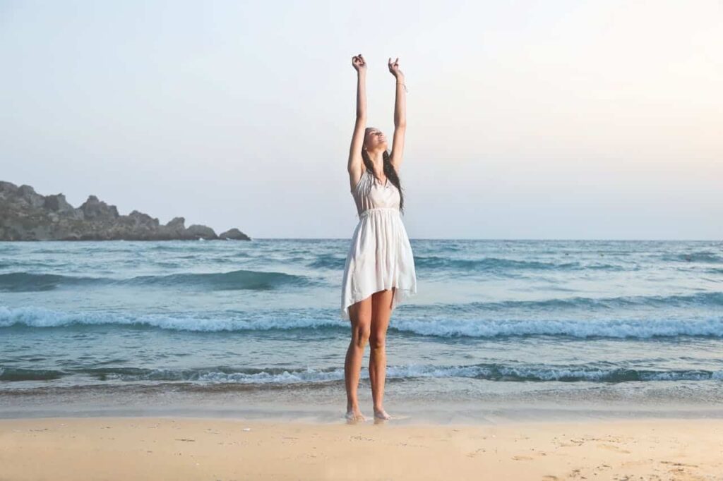 Woman in a white dress on the beach raising her hands