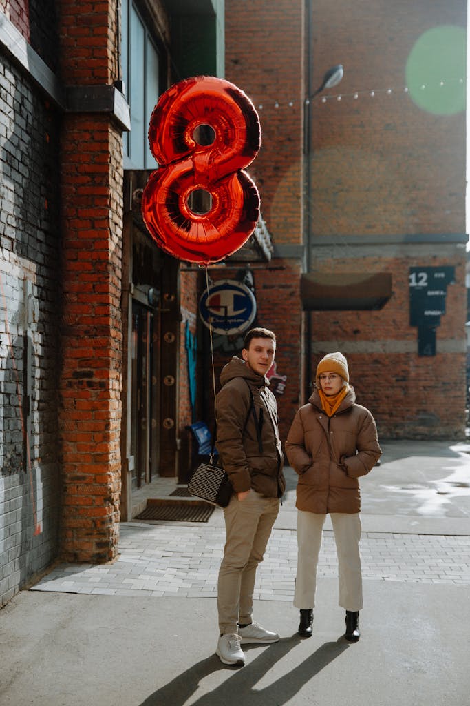 Confident couple with red number 8 foil balloon standing on urban street in cold season